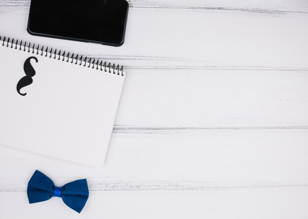 Elegant bow tie near paper mustache on notebook and smartphone