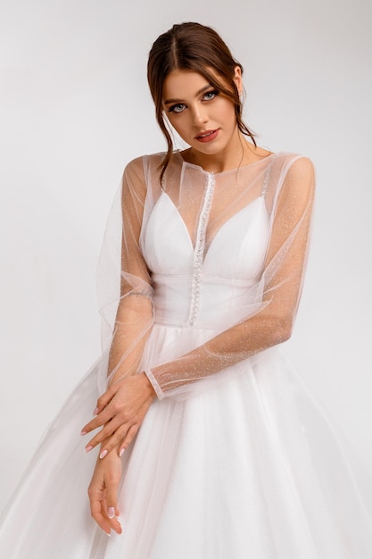 Элегантная невеста кавказка в белом свадебном платье смотрит в камеру Свадебная прическа с темным макияжем волос роскошное свадебное платье Привлекательная девушка-модель
