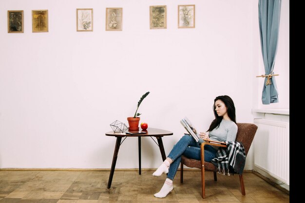 Elegant brunette dressed in casual style reads magazine sitting