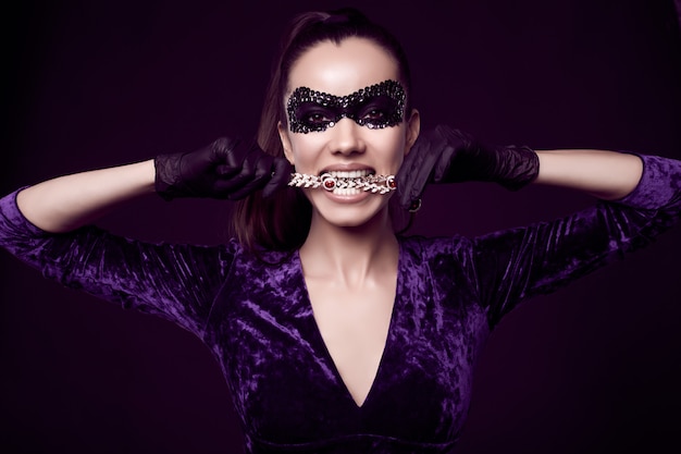 Элегантная брюнетка в красивом фиолетовом платье, маске с блестками и черных перчатках