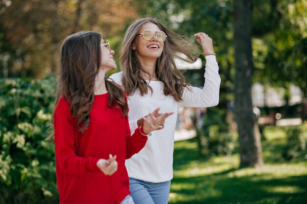 Elegant brunette woman in red shirt is using smartphone while spend time outdoor in green park