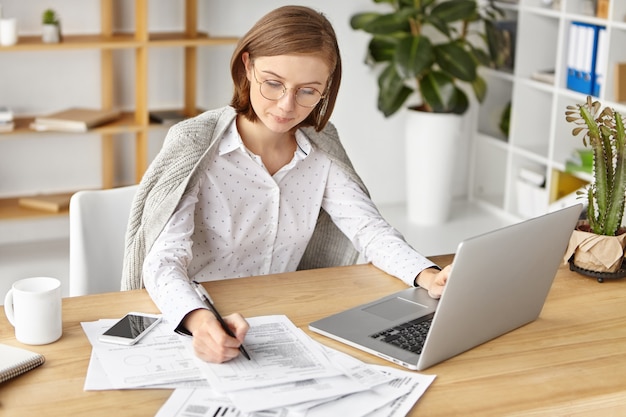 Бесплатное фото Элегантная деловая женщина, одетая официально, сидя с ноутбуком