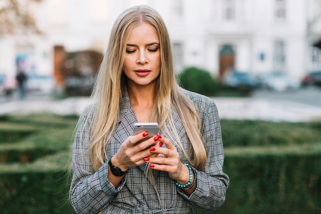 Donna di affari elegante che esamina smartphone in città