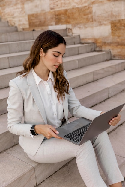 Elegant businesswoman with smartwatch working on laptop while sitting on stairs