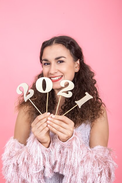 Elegante allegra giovane ragazza bruna con i capelli ricci e le spalle nude tiene un numero di legno per il concetto di nuovo anno su uno sfondo rosa