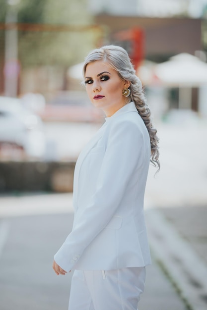 Femmina caucasica alla moda elegante in un vestito bianco grazioso e pantaloni che posano per il servizio fotografico di moda