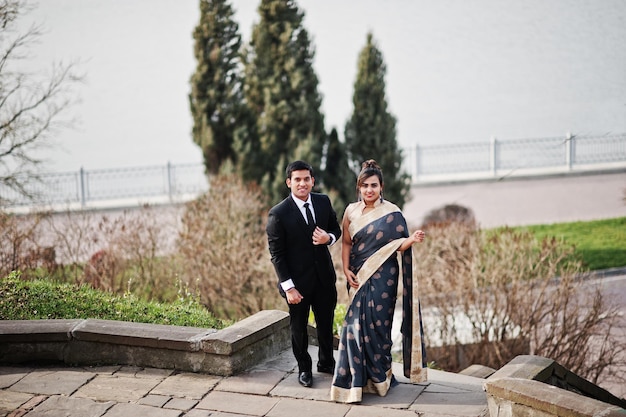 Free photo elegant and fashionable indian friends couple of woman in saree and man in suit posed on stairs against lake