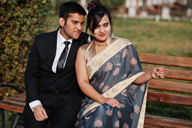 Элегантная и модная пара индийских друзей: женщина в сари и мужчина в костюме сидят на скамейке