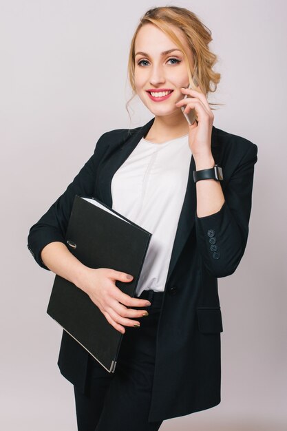 Elegant fashionable young office woman in suit, holding folder, talking on phone isolated. Cheerful mood, success, career, being busy, working, true positive emotions