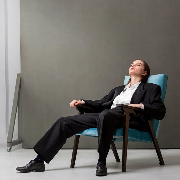 Elegant female model sitting in an armchair in a jacket suit. new feminity concept
