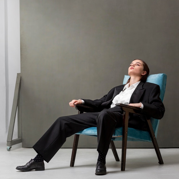 Elegant female model sitting in an armchair in a jacket suit. new feminity concept