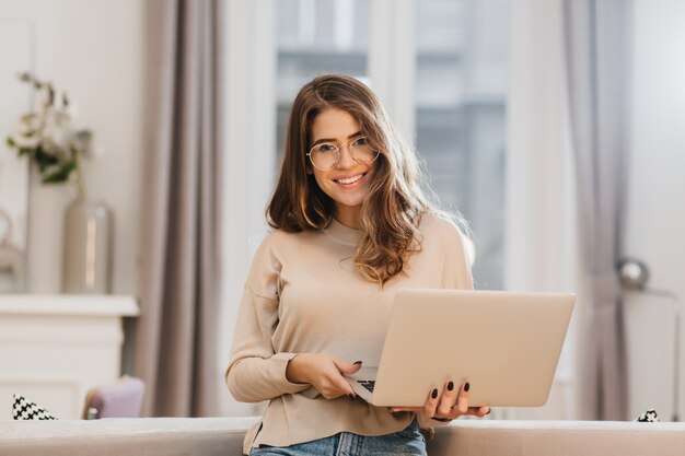 elegant female student in glasses posing with pleasure, holding laptop