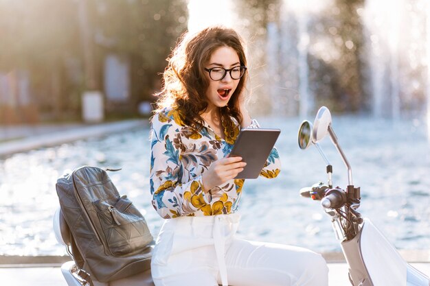 Elegant female student with leather backpack and map-case reading something with surprised face