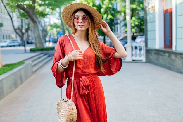 屋外を歩くサンゴのロングドレスでエレガントな豪華な女性。明るい夏の色。おしゃれなストリートルック。