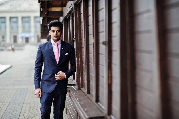 Elegant indian macho man model on suit and pink tie posed against wooden stalls