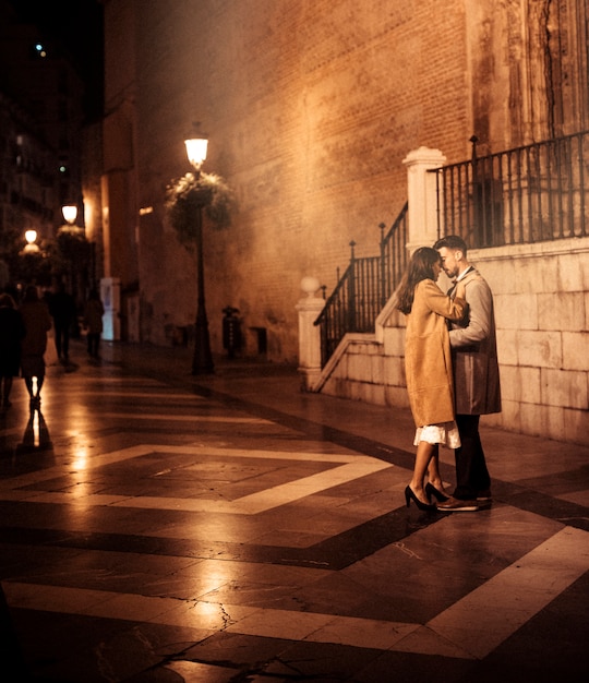 Elegant lady hugging and kissing with young guy on street