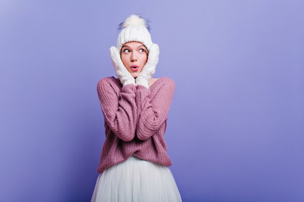 Elegant lady in mittens and hat expressing amazement. Shocked young woman in trendy hat posing with surprised face.