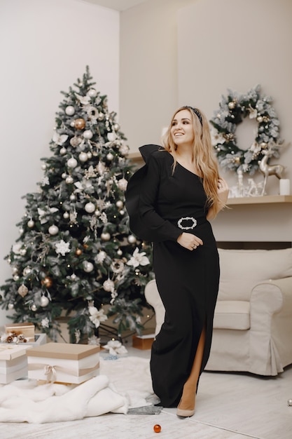 Elegant lady near Christmas tree. Woman in a room. Famale in a elegant black dress.