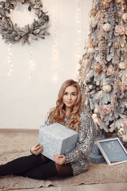 Signora elegante vicino all'albero di natale. donna in una stanza. famale in un vestito d'argento.