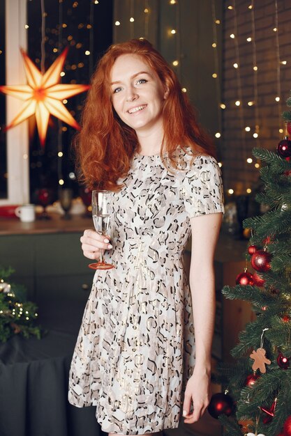クリスマスの木の近くのエレガントな女性。シャンパンで家にいる女性。