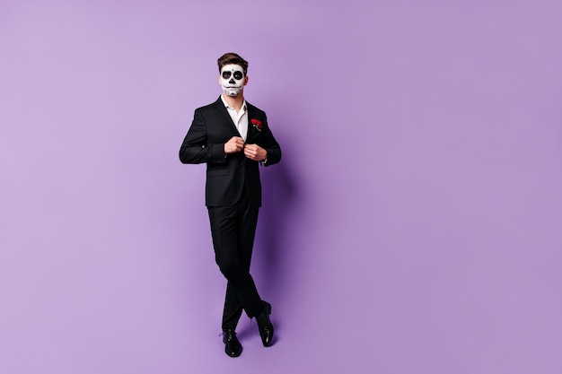검은 색 클래식 재킷을 단추로 누르고 가장 무도회 마스크에 편안한 스튜디오에서 포즈를 취하는 우아한 남자.
