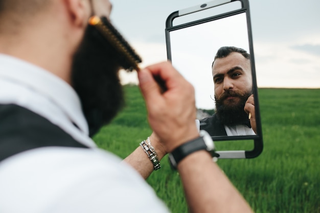 Elegant man holding a mirror and combing his beard