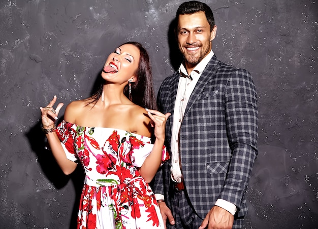 elegant man in suit with beautiful woman posing near gray wall