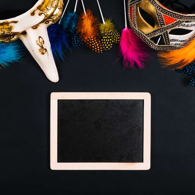 Free photo elegant masks and bright feathers near blackboard