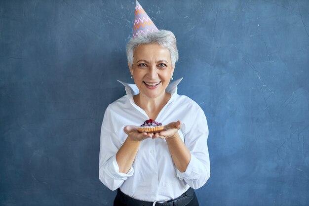 Elegant middle aged in white shirt celebrating anniversary posing isolated with freshly baked pie, having joyful facial expression