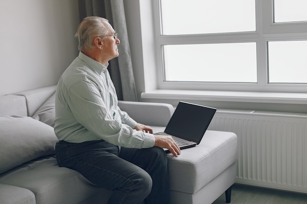 Elegant old man sitting at home and using a laptop