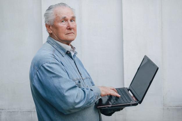 Elegant old man standing on gray background and using a laptop