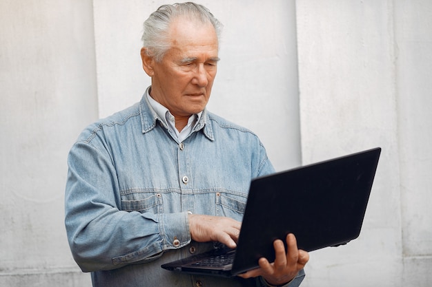 Элегантный старик стоит и использует ноутбук