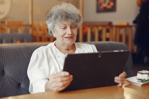 Элегантная пожилая женщина сидит в кафе и использует ноутбук