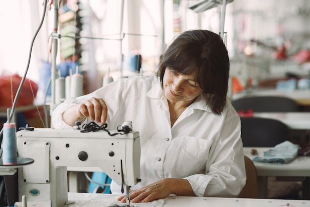 Elegant old woman sitting in studio and sew cloth