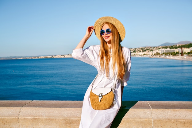 Элегантная симпатичная блондинка позирует на смотровой площадке Ниццы, Франция, в стильном летнем наряде