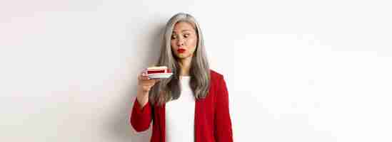 Free photo elegant senior woman in red blazer wants take bite of sweet cake looking with tempted face at desser