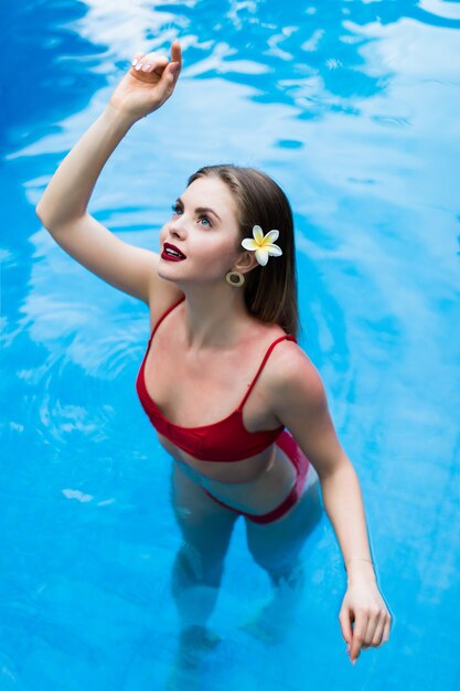 태양 무두질 슬림하고 매끈한 몸에 빨간 비키니 입은 우아한 섹시한 여자가 수영장에서 수영