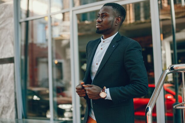 elegant and stylish black guy in a blue shirt and black jacket standing in the summer city