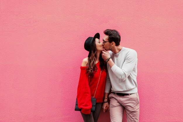 Элегантная стильная влюбленная пара, держащая руки и смотрящая друг на друга с удовольствием. Длинноволосая женщина в красном вязаном свитере с парнем позирует.