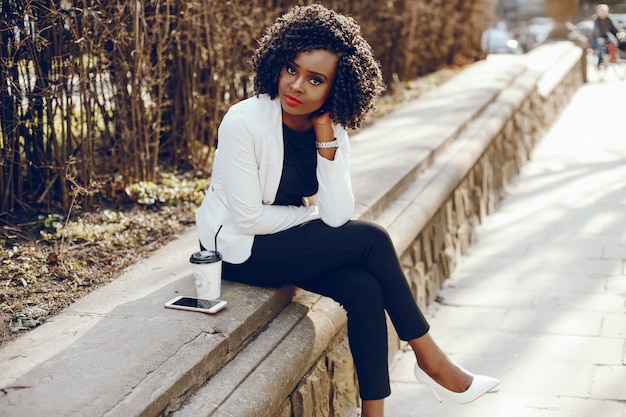 elegant and stylish dark-skinned girl with curly hair and in a white jacket sitting