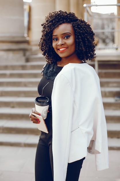 elegant and stylish dark-skinned girl with curly hair and in a white jacket walking around