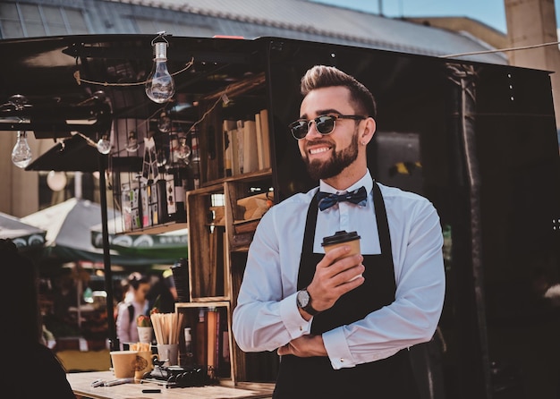 Elegant trendy barista in glasses has a coffee break at his own coffeeshop and enjoying coffee.