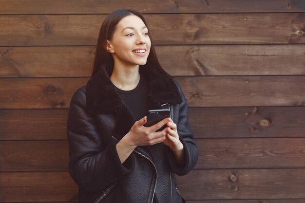 Elegant woman in a black jacket standing on a brown wall