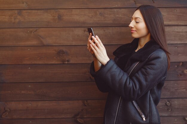 Elegant woman in a black jacket standing on a brown wall