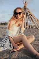 Free photo elegant woman in black sunglasses sitting on the beach at sunset