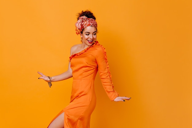 Elegant woman in dress with bare shoulder coquettishly posing on orange space.