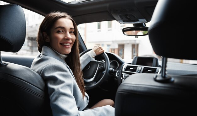 Элегантная женщина-водитель, глядя на заднее сиденье, улыбаясь счастливой