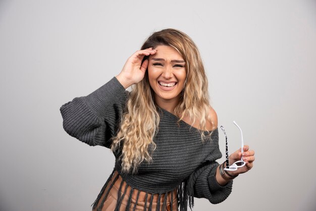 Elegant woman in gray sweater holding glasses happily.