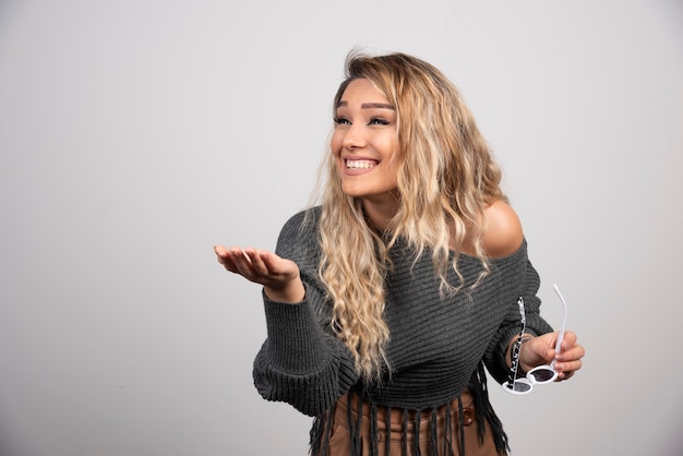 Elegant woman in gray sweater holding glasses happily.