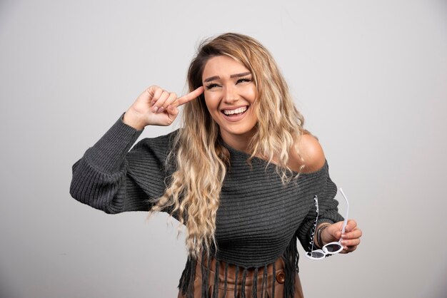 Elegant woman in gray sweater holding glasses happily.